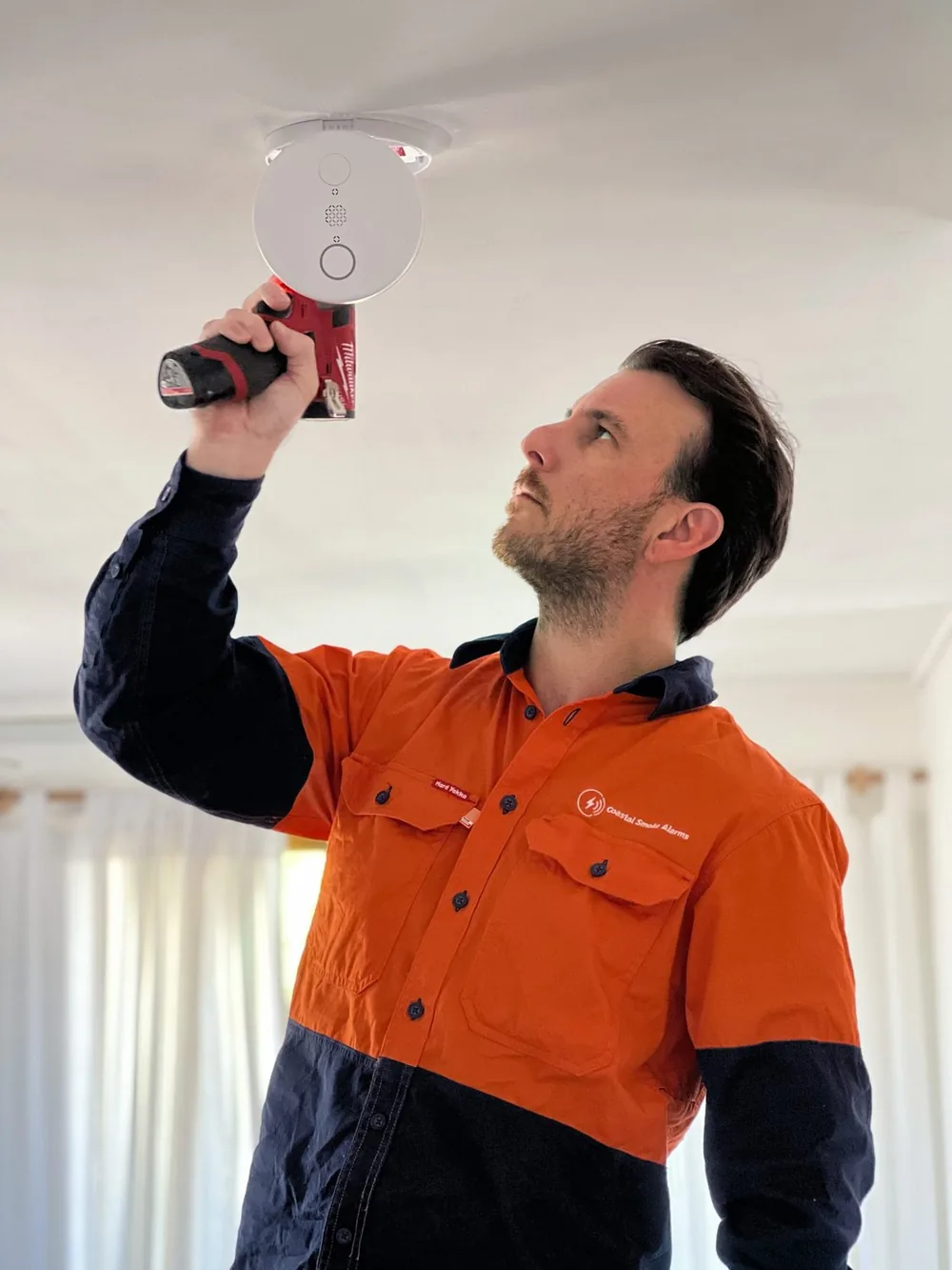 Ryan Tait, licensed electrician, installing a photoelectric smoke alarm in a Gold Coast home